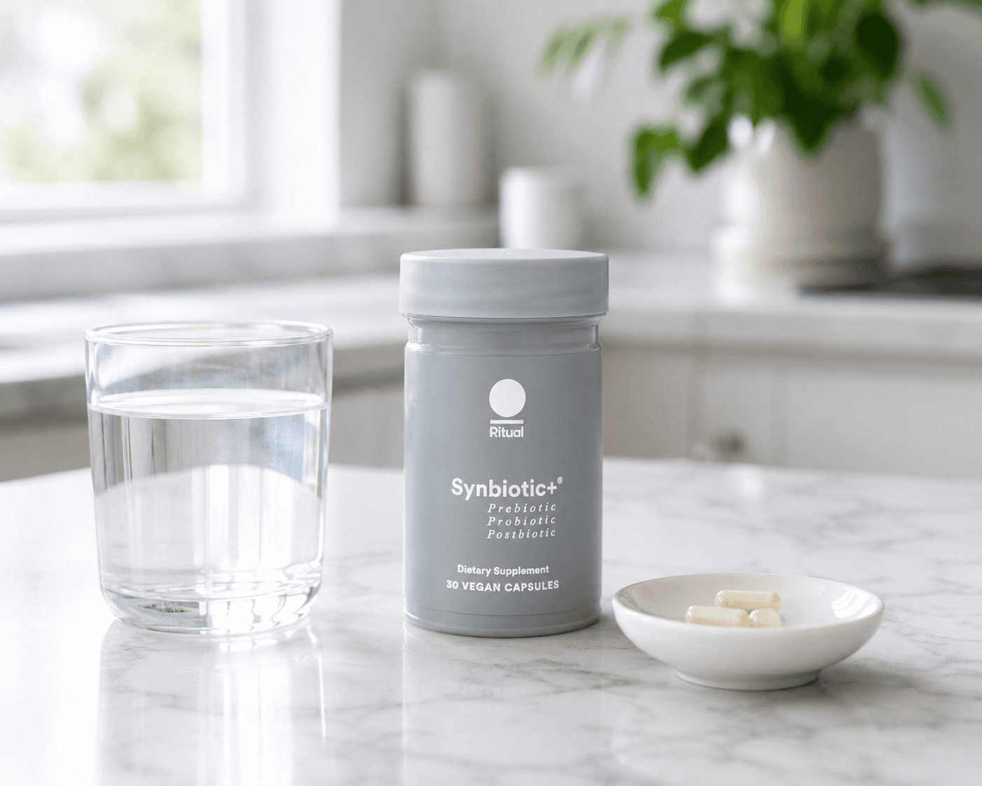 Bottle of Ritual Synbiotic+ with capsules and a glass of water on a kitchen counter