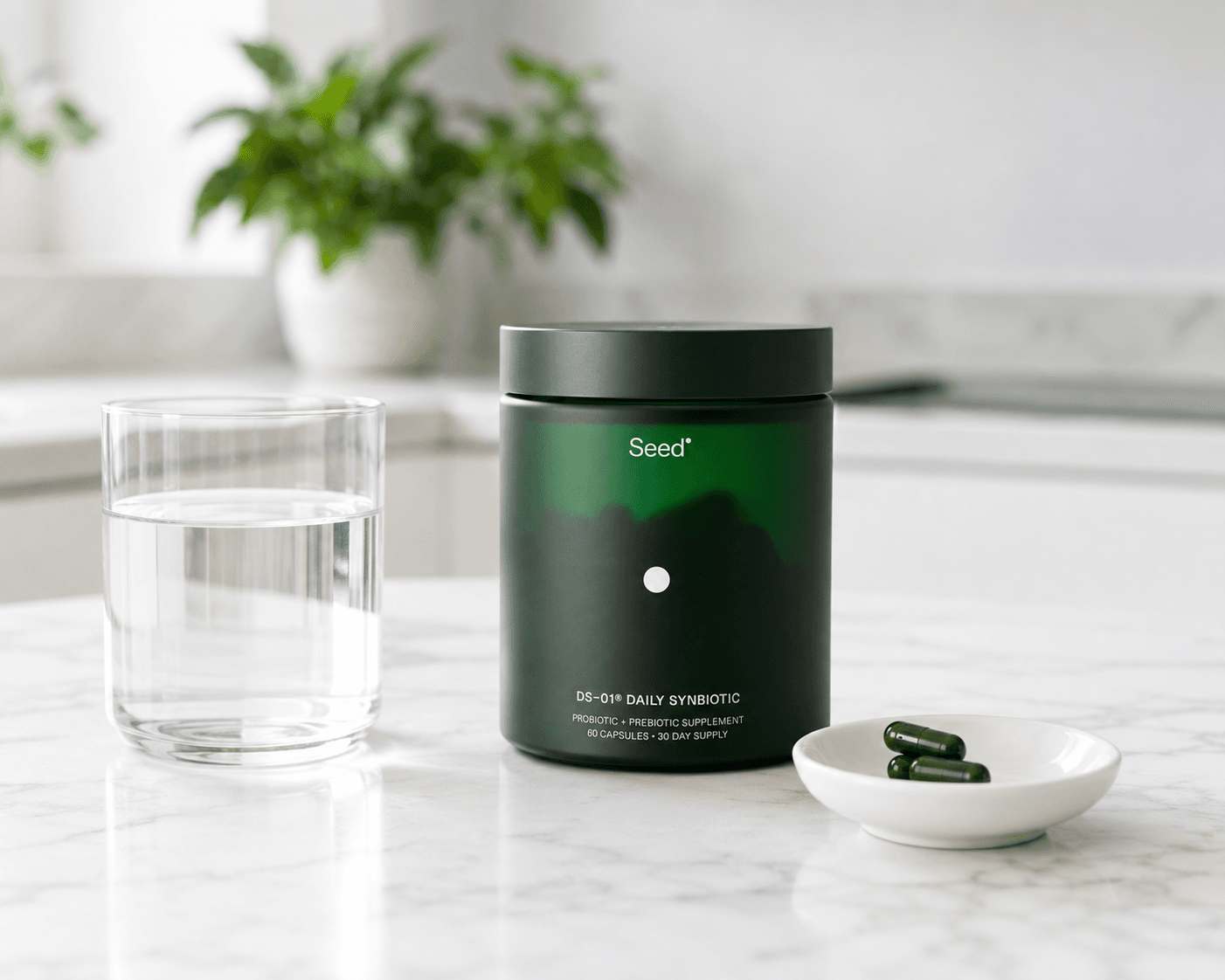 Jar of Seed Daily Synbiotic with capsules and a glass of water on a kitchen counter